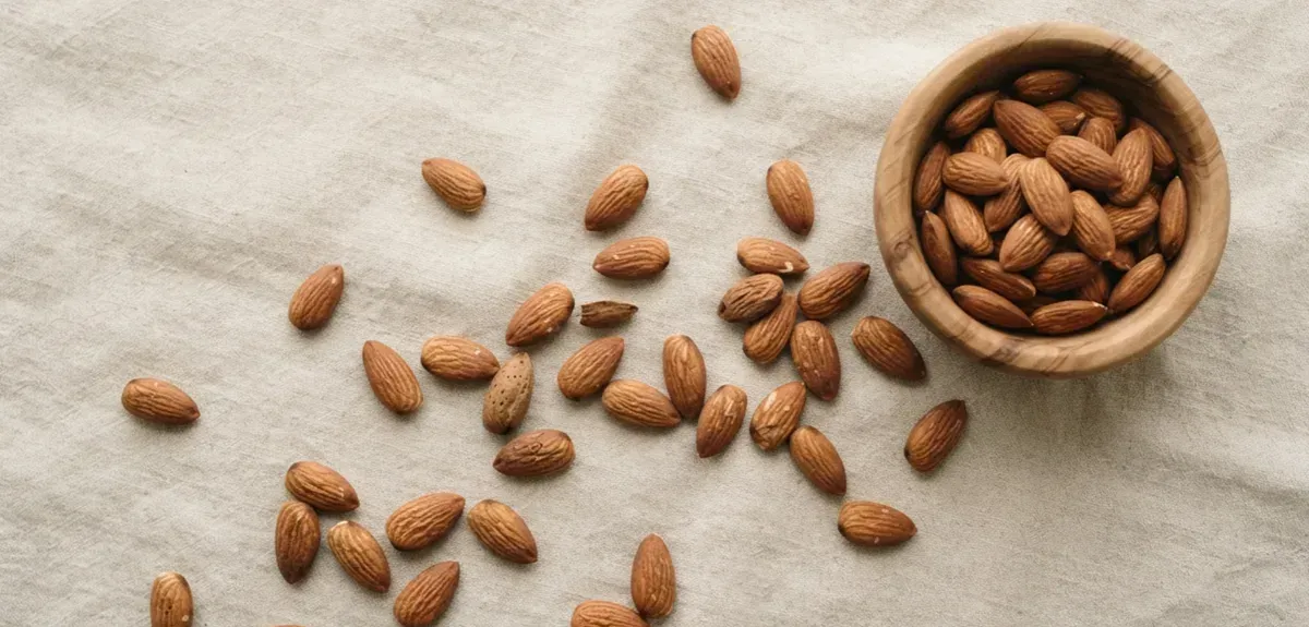 A small bowl of raw almonds beside a glass of water