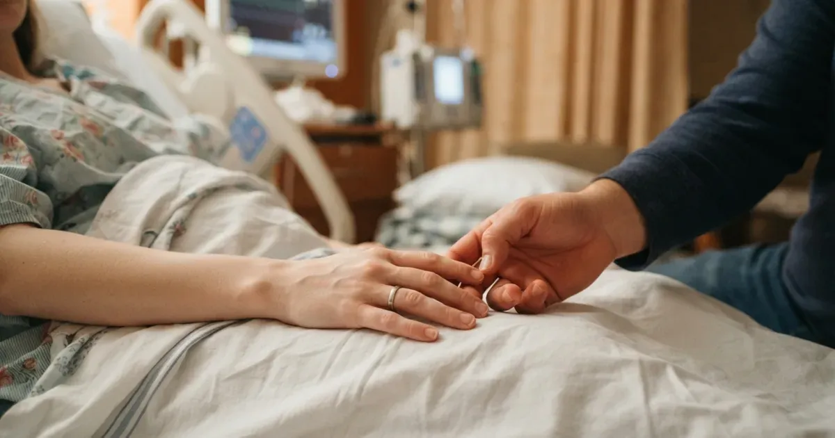 Two hands clasped together beside a hospital bed